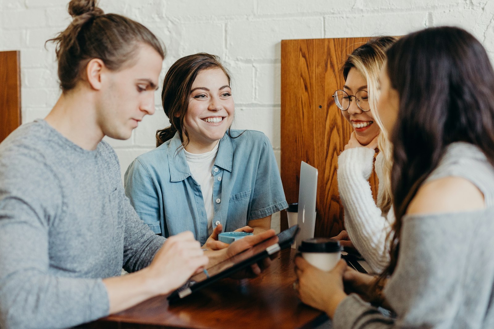 A diverse, casually-dressed team sharing a laugh over a tablet in a collaborative workspace.
